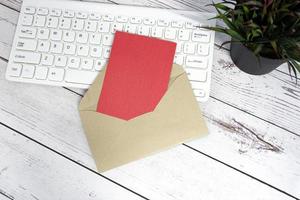 note rouge à l'intérieur d'une enveloppe brune avec clavier et plante en pot sur un bureau en bois.