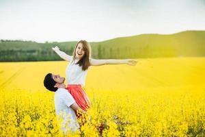 je me sens libre joyeuse jeune femme lève les mains étant sur les mains de l'homme, pose ensemble sur le champ de fleurs jaunes par temps ensoleillé d'été. un couple romantique s'amuse en plein air. notion de relations. photo