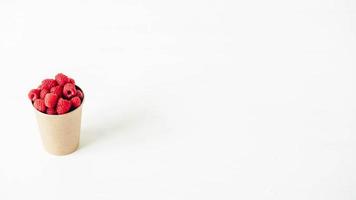 Framboises rouges fraîches dans une tasse de papier sur un fond de tableau blanc photo