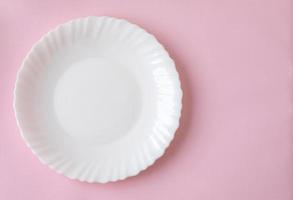 assiette blanche avec une ombre douce sur un fond de surface rose clair photo