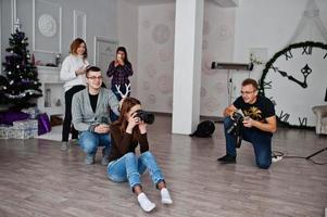 l'équipe de deux photographes prenant des photos en studio derrière trois autres ouvriers. photographe professionnel sur le travail. l'un d'eux plaisante et tient des cornes au-dessus de la tête.