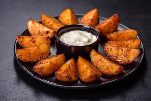 quartiers de pommes de terre au four avec fromage et herbes et sauce tomate sur fond sombre photo