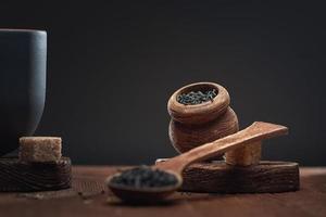 thé sec dans des cuillères en bois et dans un pot en bois et des morceaux de sucre de canne sur la table, sur fond sombre. photo