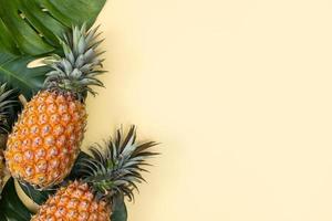 bel ananas sur des feuilles de monstera de palmiers tropicaux isolés sur fond jaune pastel clair, vue de dessus, à plat, au-dessus des fruits d'été. photo