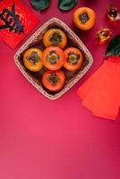 vue de dessus de kakis sucrés frais avec des feuilles sur fond de table rouge pour le nouvel an lunaire chinois photo