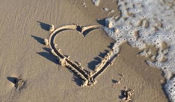 une belle forme de coeur peinte dans le sable d'une plage de la mer baltique avec quelques vagues d'eau. photo