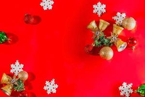 concept de fond de noël. vue de dessus des cloches dorées de noël avec décoration de boules, branches d'épinette, étoile et flocons de neige sur fond rouge. photo