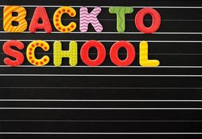 concept de retour à l'école avec des lettres magnétiques colorées sur un tableau noir sur fond noir. il y a un champ de texte libre. photo