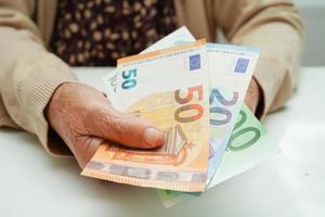 une femme âgée à la retraite tenant des billets en euros et s'inquiète des dépenses mensuelles et du paiement des frais de traitement. photo