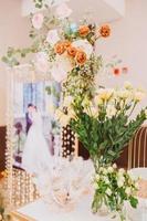 composition florale pour mariage d'été, faite de roses et de branches vertes sur une table de dîner au restaurant. , verre et assiettes dans le restaurant à l'extérieur par une journée venteuse avec effet de grain de film photo