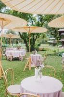 composition florale pour mariage d'été, faite de roses et de branches vertes sur une table de dîner au restaurant. , verre et assiettes dans le restaurant à l'extérieur par une journée venteuse avec effet de grain de film photo