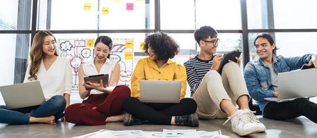 groupe de jeunes gens d'affaires créatifs asiatiques heureux ou étudiant hipster utilisant des appareils électroniques connexion tablette et ordinateur portable ensemble dans un bureau moderne. concept de style de vie créatif des jeunes photo