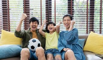 famille asiatique regardant des matchs de football à la télévision et réagissant avec joie lorsque l'équipe tire le ballon dans le but. photo