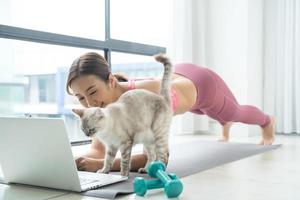 jeune belle femme asiatique s'entraînant à la maison avec un chat et regardant un tutoriel en ligne sur un ordinateur portable. photo