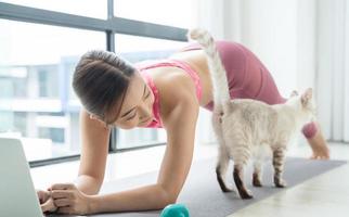 jeune belle femme asiatique s'entraînant à la maison avec un chat et regardant un tutoriel en ligne sur un ordinateur portable. photo