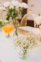 composition florale pour mariage d'été, faite de roses et de branches vertes sur une table de dîner au restaurant. , verre et assiettes dans le restaurant à l'extérieur par une journée venteuse avec effet de grain de film photo