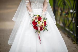 jeune fille mariée en séjour dans la rue de la ville et attend le marié avec bouquet de roses rouges et blanches photo