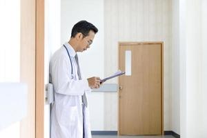 un médecin de sexe masculin asiatique regarde le dossier médical du patient après avoir effectué une visite de salle pour un meilleur examen de guérison et un futur concept de traitement du plan de soins infirmiers photo