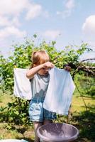 petite fille d'âge préscolaire aide à faire la lessive. enfant lave les vêtements dans le jardin