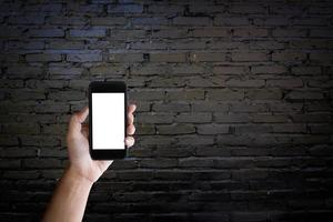 homme tenant un écran vierge d'un smartphone sur le vieux mur de briques noires. photo