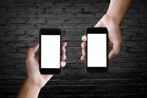 deux mains tenant l'écran vide d'un smartphone sur le vieux mur de briques noires. photo