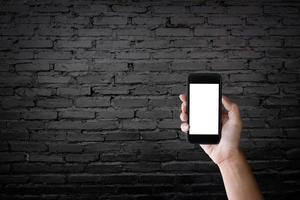 homme tenant un écran vierge d'un smartphone sur le vieux mur de briques noires. photo