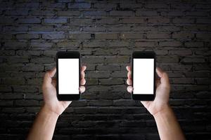 les mains de l'homme tenant l'écran vide d'un smartphone sur le vieux mur de briques noires. photo
