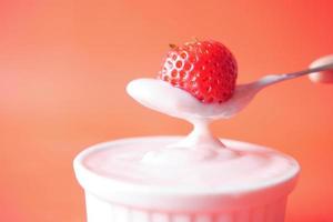 yaourt et fraise sur une cuillère sur fond rouge photo