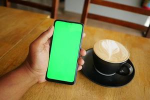 tenant un processeur de café et utilisant un téléphone intelligent avec écran vert photo