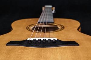 texture bois du pont inférieur de la guitare acoustique à six cordes sur fond noir. forme de guitare photo