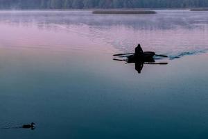 silhouette d'homme dans un bateau tôt le matin. aube rose avec des canards photo
