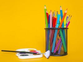 crayons de couleur dans un étui à crayons sur fond jaune avec une feuille de papier blanche et des peintures