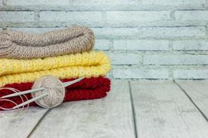 tricots multicolores pliés avec une pelote de fil et des aiguilles à tricoter sur un fond en bois clair. concept d'artisanat, vente