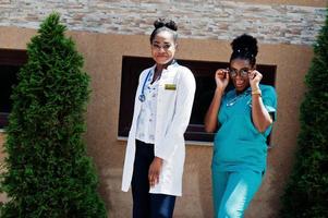 deux médecins afro-américains féminins en blouse de laboratoire avec stéthoscope posés en plein air contre la clinique. photo