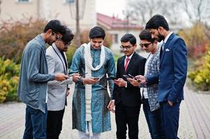 groupe de six hommes indiens d'asie du sud en vêtements traditionnels, décontractés et professionnels debout et regardant ensemble des téléphones portables. photo