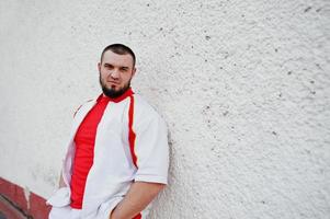 jeune homme musclé barbu brutal porte un costume de sport blanc avec une chemise rouge. photo