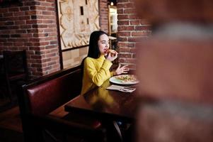 drôle de fille brune en pull jaune, manger de la pizza au restaurant. photo