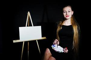 belle femme artiste peintre avec pinceaux et toile à l'huile posant en studio isolé sur noir. photo