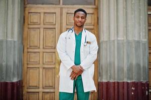 médecin afro-américain mâle au sarrau de laboratoire avec stéthoscope extérieur contre la porte de la clinique. photo