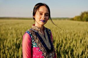 tendre fille indienne en sari, avec des lèvres violettes maquillées posées sur le terrain au coucher du soleil. modèle indien à la mode. photo