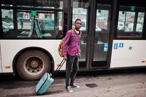 homme afro-américain en chemise à carreaux, avec valise et sac à dos. voyageur homme noir contre le bus. photo