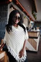 élégante fille afro-américaine à lunettes de soleil posées au café moderne. photo