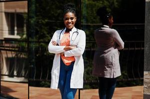 femme médecin afro-américaine en blouse de laboratoire avec stéthoscope posé en plein air contre la clinique. photo
