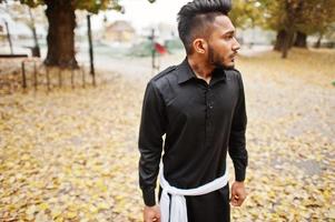 homme élégant indien en vêtements traditionnels noirs posés en plein air contre l'humeur d'automne. photo