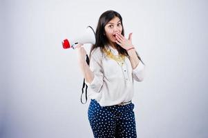 portrait d'une jeune femme en pantalon bleu et chemisier blanc posant avec mégaphone en studio. photo