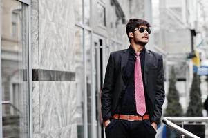 jeune homme indien en costume, cravate et lunettes de soleil posés à l'extérieur. photo