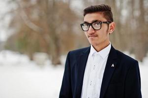 portrait en gros plan d'un étudiant indien élégant en costume et lunettes posé à la journée d'hiver en plein air. photo