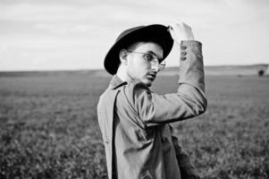 homme élégant à lunettes, veste marron et chapeau posé sur champ vert. photo