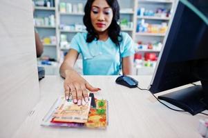 pharmacien afro-américain travaillant en pharmacie à la pharmacie hospitalière. soins de santé africains. caissier détenant de l'argent en euros. photo