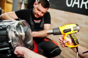 le travailleur du service automobile a mis un film anti-gravier sur une carrosserie de voiture rouge à l'atelier de détail du véhicule. protection de voiture avec des films spéciaux. photo